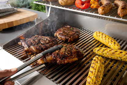 AOG 24-inch gas grill cooking steak and corn in outdoor kitchen